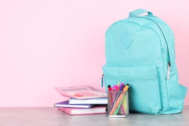 Photo of Backpack with different school stationery on light grey table against pink background