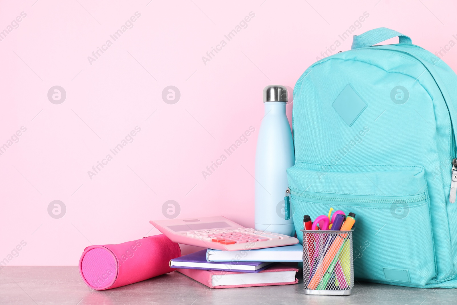 Photo of Backpack with different school stationery and bottle on light grey table against pink background. Space for text