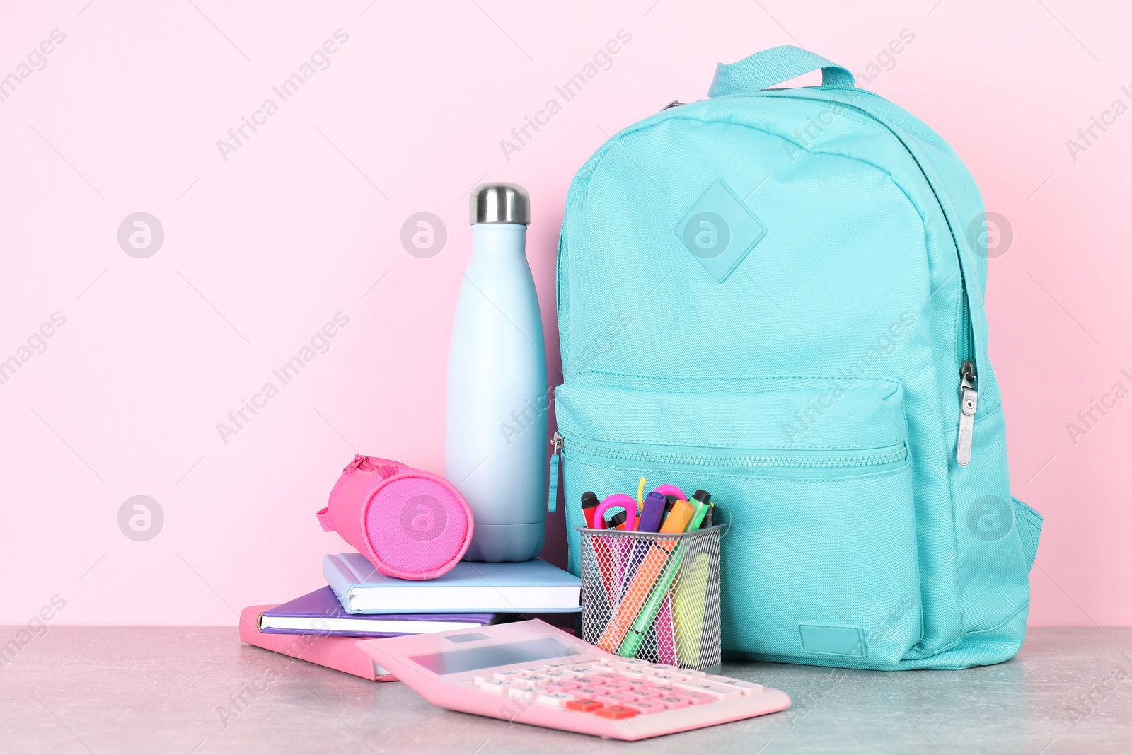 Photo of Backpack with different school stationery and bottle on light grey table against pink background