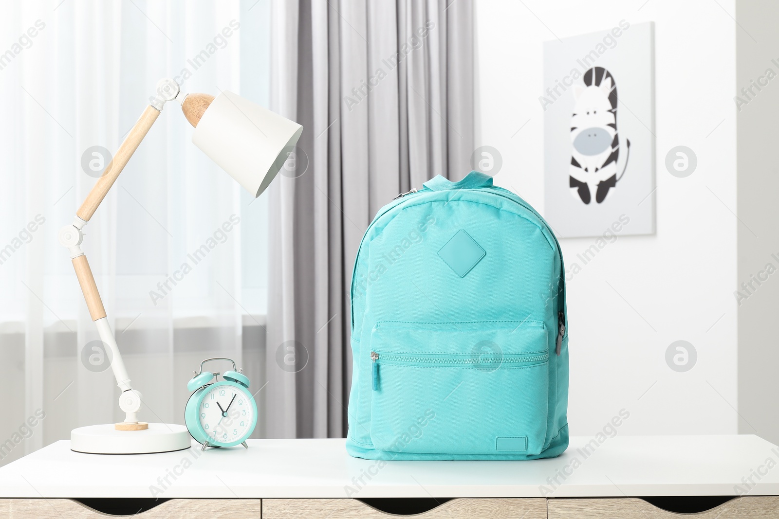 Photo of Backpack with different school stationery and alarm clock on desk in room