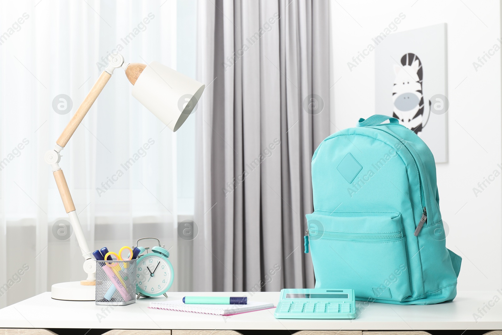 Photo of Backpack with different school stationery and alarm clock on desk in room