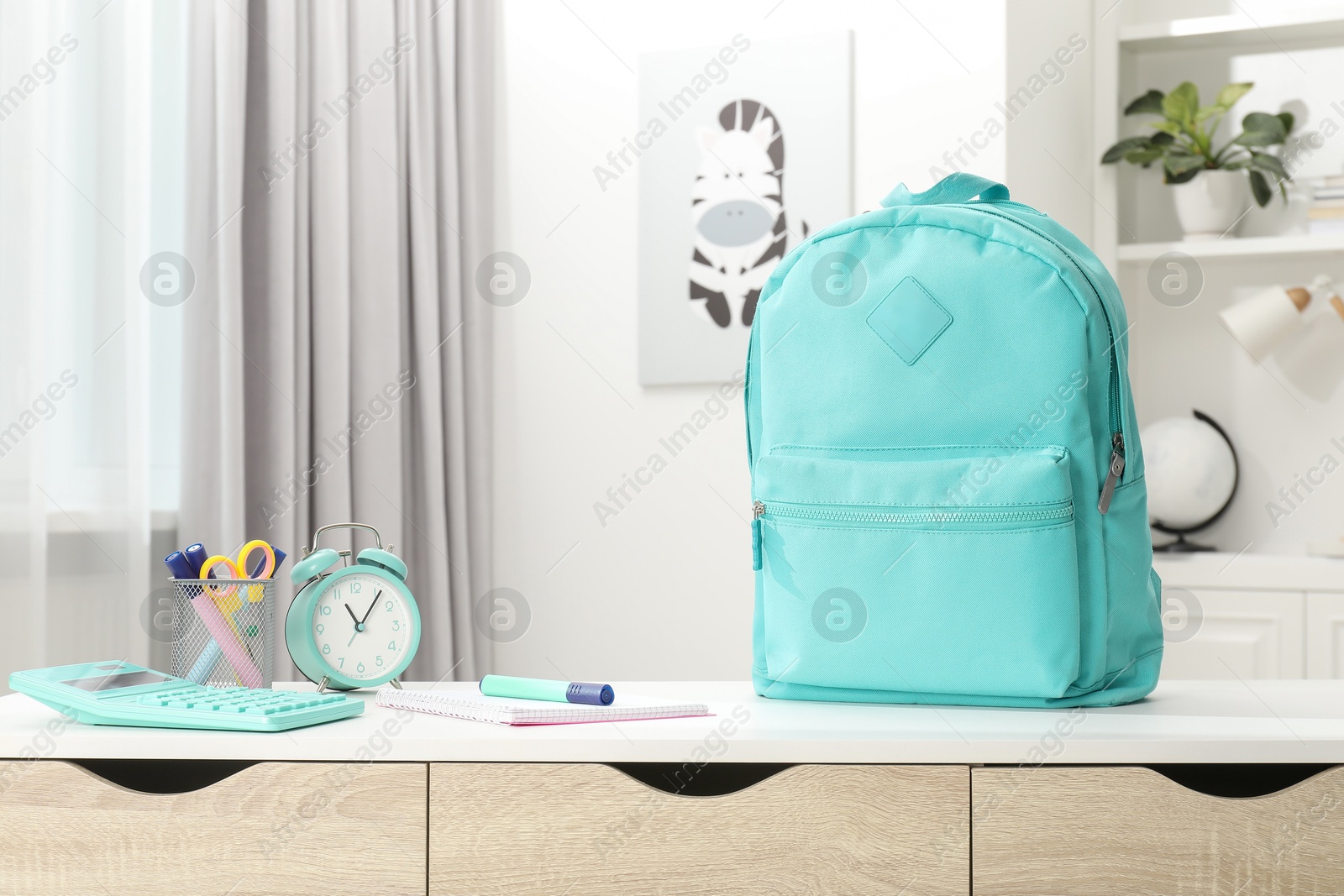 Photo of Backpack with different school stationery and alarm clock on desk in room