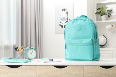 Photo of Backpack with different school stationery and alarm clock on desk in room