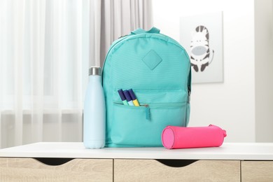 Photo of Backpack with different school stationery and bottle on desk in room