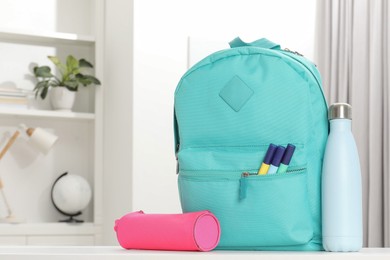 Photo of Backpack with different school stationery and bottle on desk in room