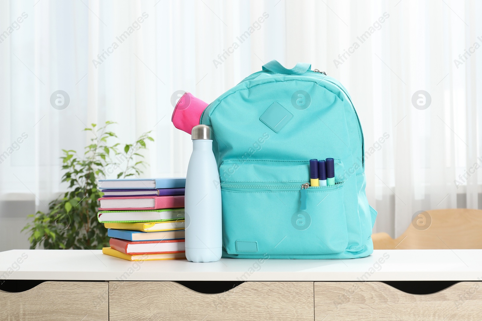 Photo of Backpack with different school stationery and bottle on desk in room