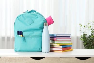 Photo of Backpack with different school stationery and bottle on desk in room