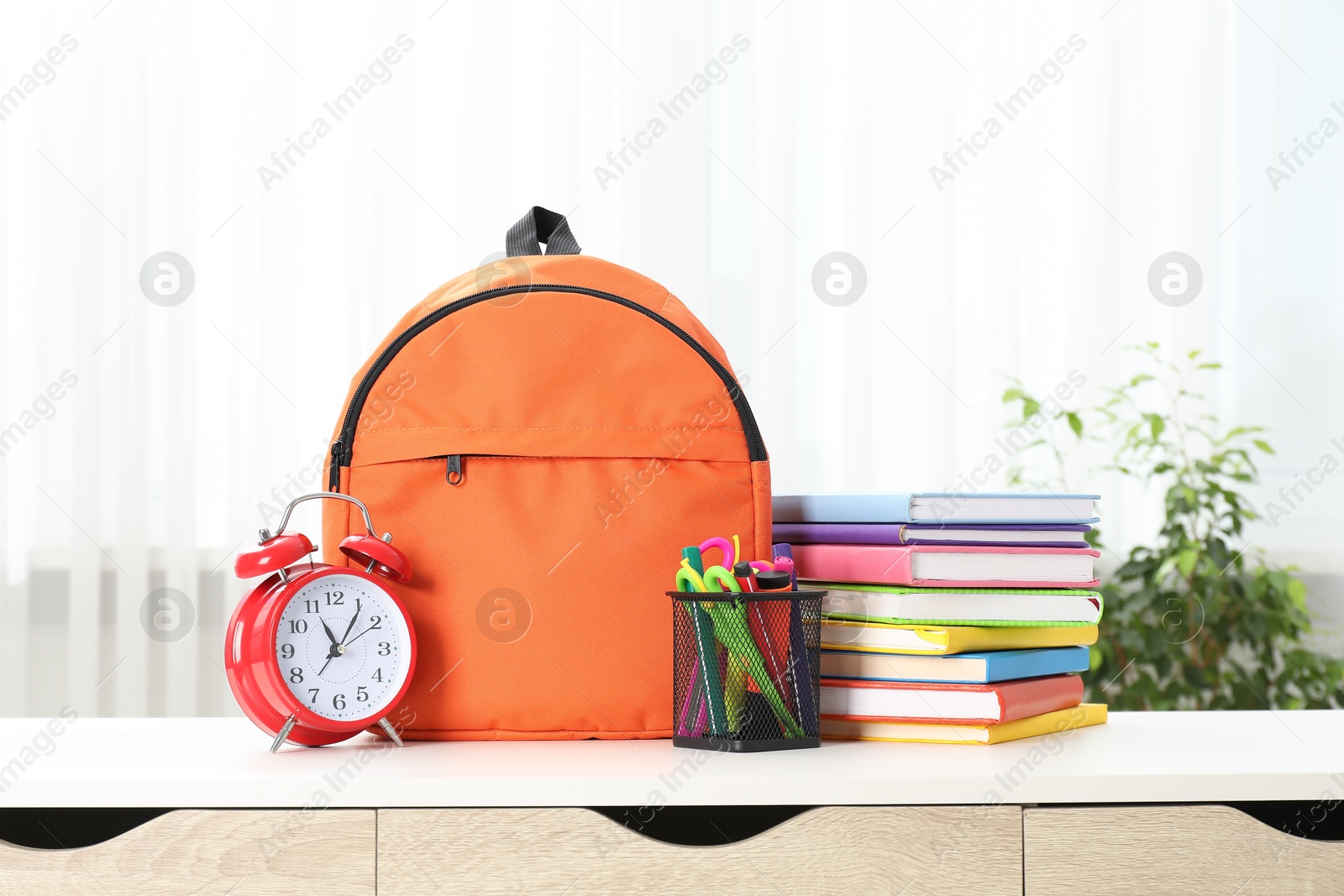 Photo of Backpack with different school stationery and alarm clock on desk in room