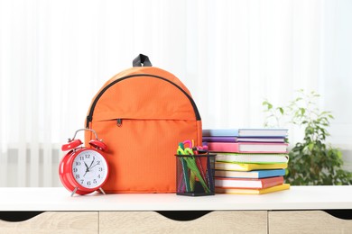 Photo of Backpack with different school stationery and alarm clock on desk in room