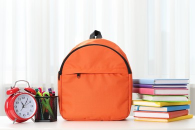 Photo of Backpack with different school stationery and alarm clock on desk in room