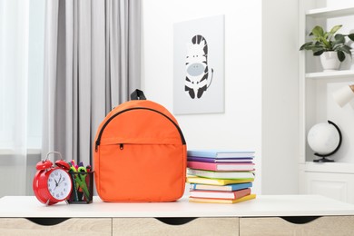 Photo of Backpack with different school stationery and alarm clock on desk in room