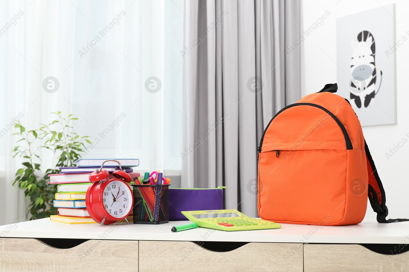 Photo of Backpack with different school stationery and alarm clock on desk in room. Space for text