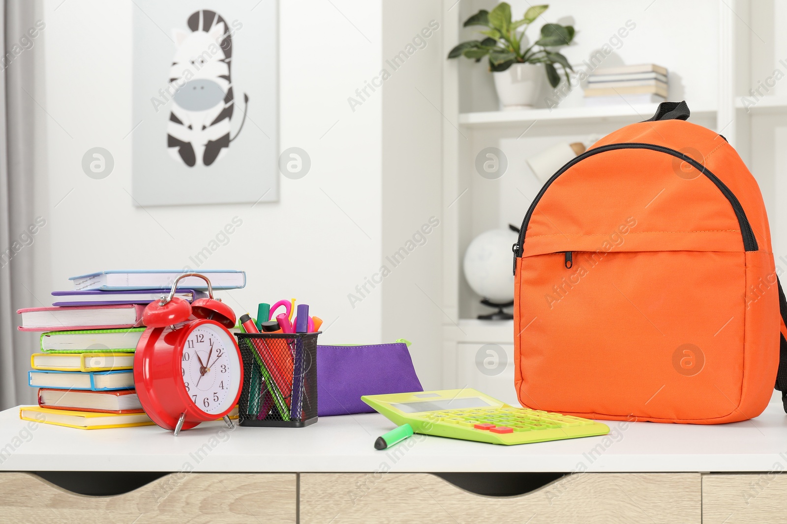 Photo of Backpack with different school stationery and alarm clock on desk in room