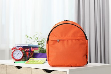 Photo of Backpack with different school stationery and alarm clock on desk in room