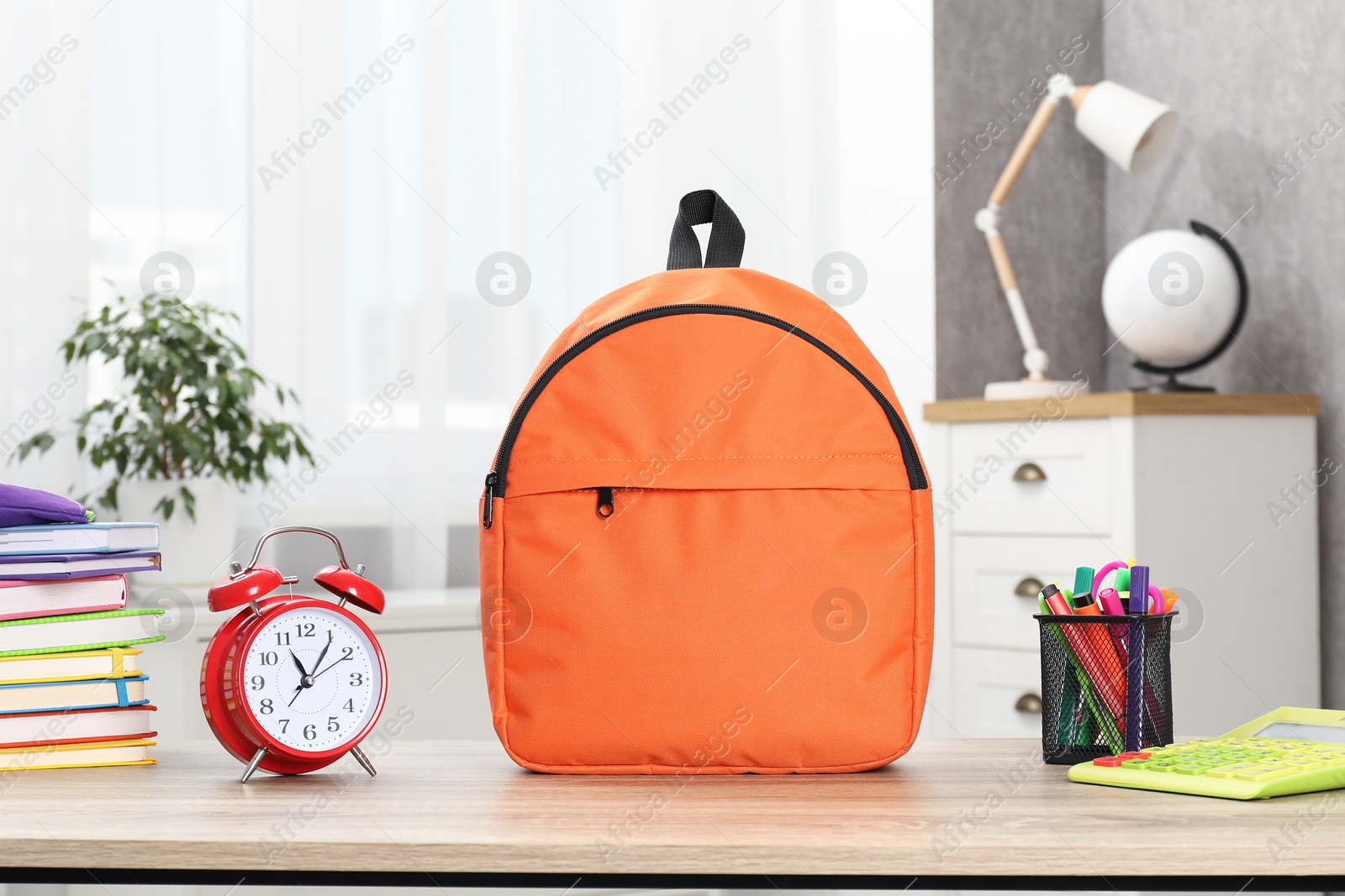 Photo of Backpack with different school stationery and alarm clock on desk in room