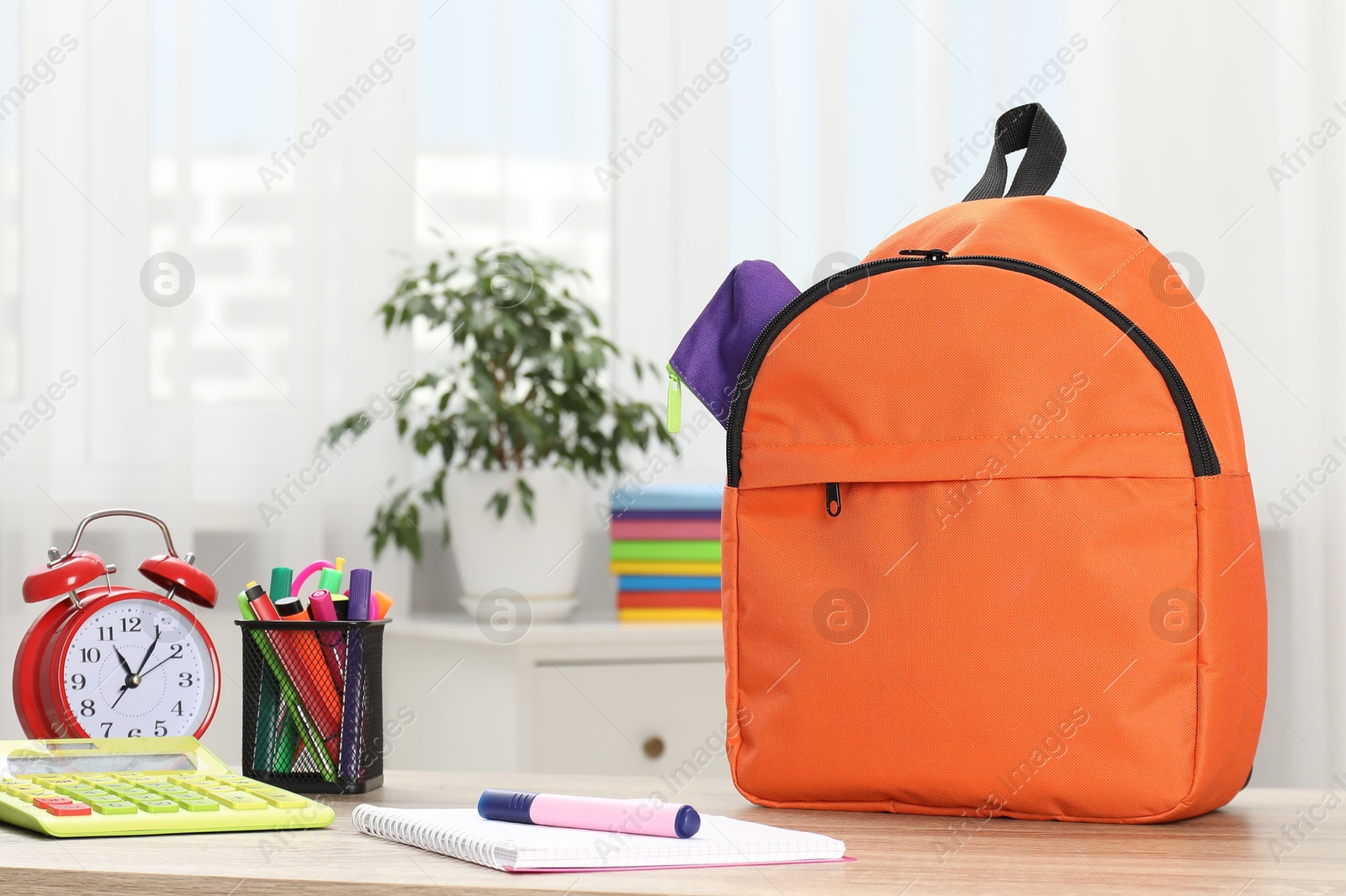 Photo of Backpack with different school stationery and alarm clock on desk in room. Space for text