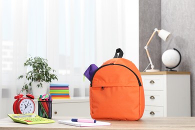 Photo of Backpack with different school stationery and alarm clock on desk in room