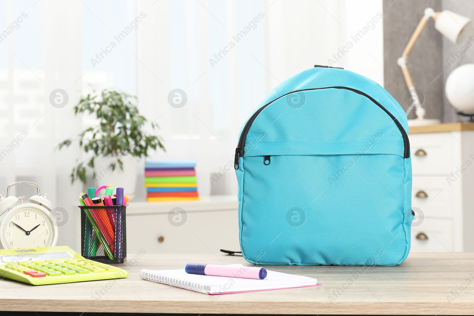 Photo of Backpack with different school stationery and alarm clock on desk in room. Space for text