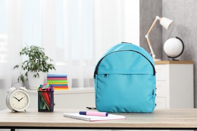 Photo of Backpack with different school stationery and alarm clock on desk in room. Space for text