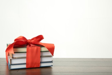 Photo of Stack of books with red ribbon as gift on wooden table against white background, space for text