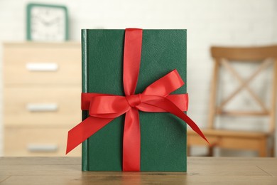 Photo of Book with red ribbon as gift on wooden table indoors