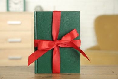 Photo of Book with red ribbon as gift on wooden table indoors