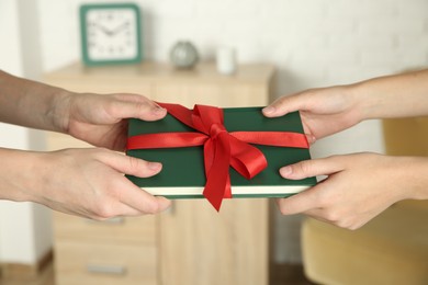 Photo of Woman gifting her friend book tied with red ribbon indoors, closeup