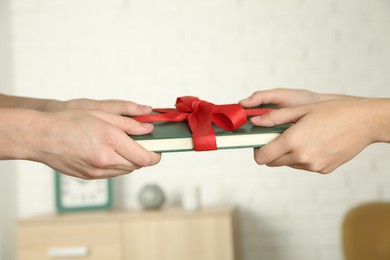 Photo of Woman gifting her friend book tied with red ribbon indoors, closeup