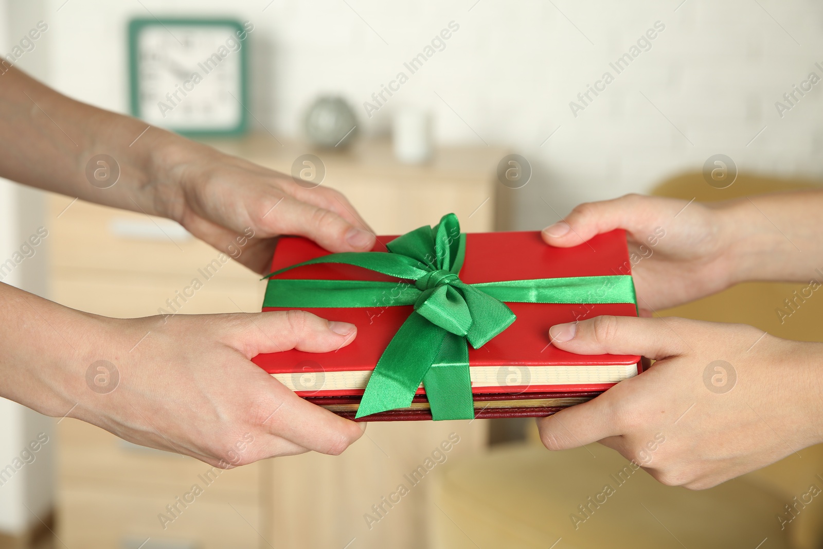 Photo of Woman gifting her friend book tied with red ribbon indoors, closeup