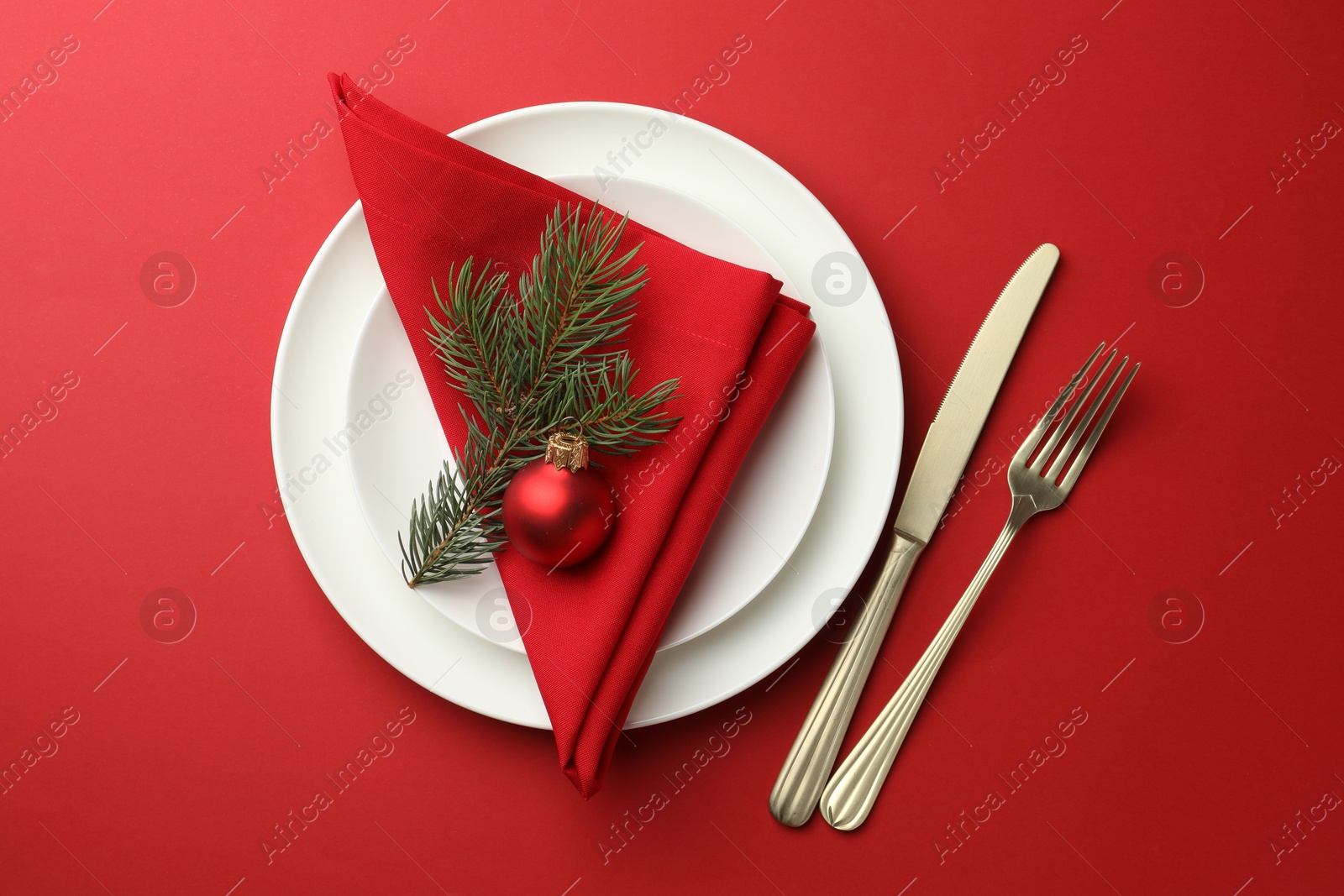 Photo of Beautiful Christmas setting with plates, elegant cutlery and festive decor on red table, flat lay