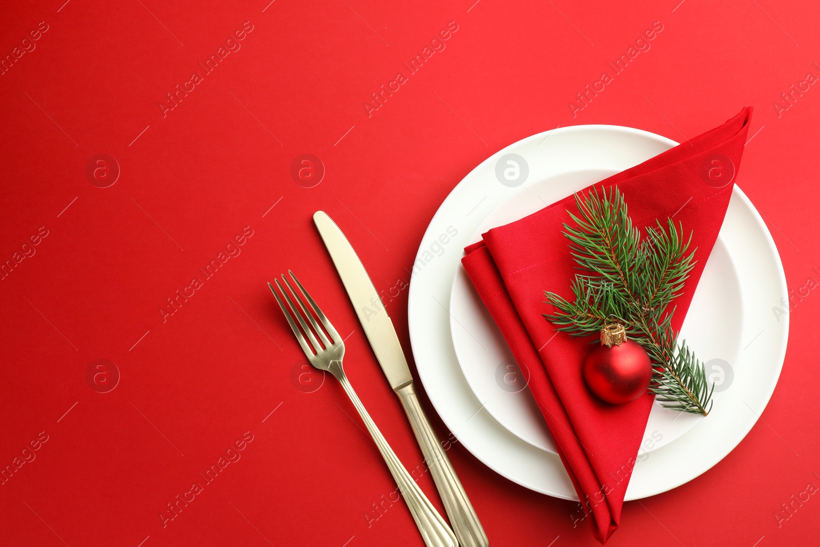 Photo of Beautiful Christmas setting with plates, elegant cutlery and festive decor on red table, flat lay. Space for text