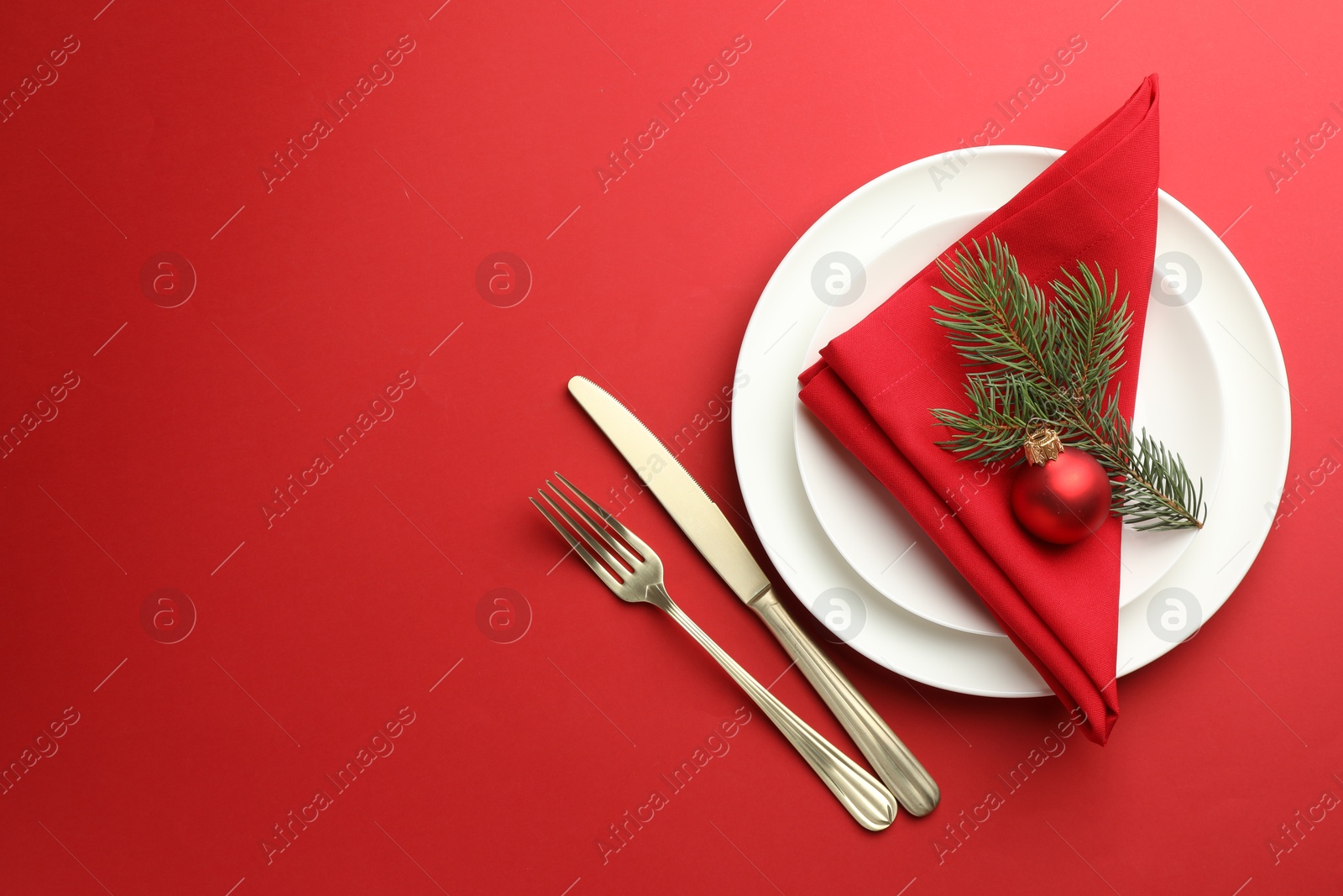 Photo of Beautiful Christmas setting with plates, elegant cutlery and festive decor on red table, flat lay. Space for text