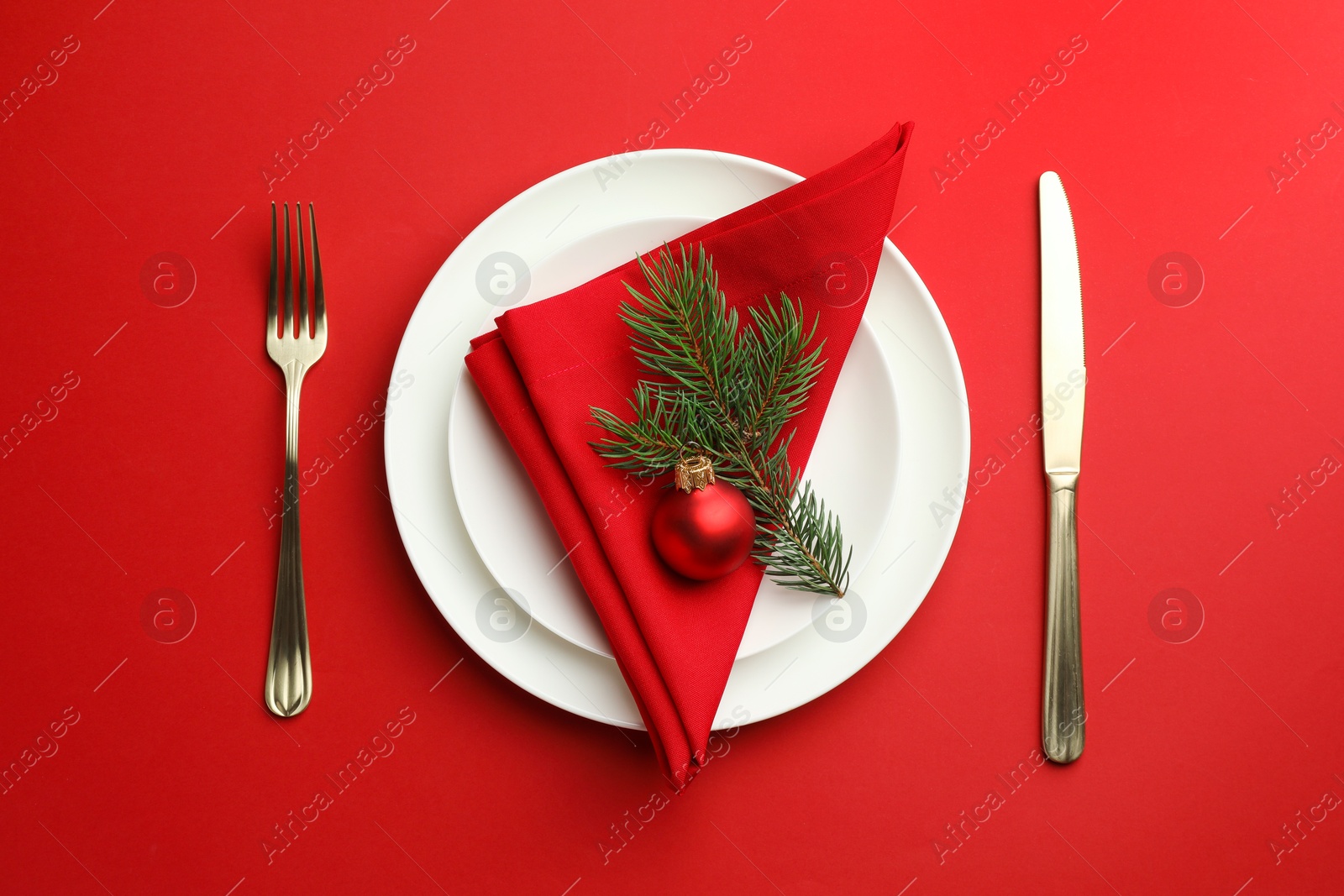 Photo of Beautiful Christmas setting with plates, elegant cutlery and festive decor on red table, flat lay