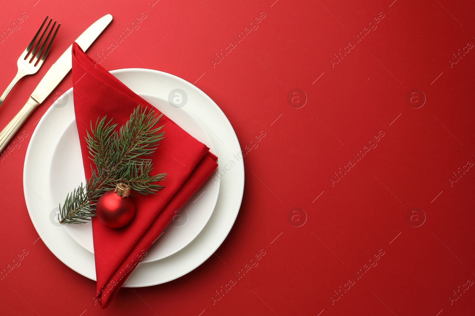 Photo of Beautiful Christmas setting with plates, elegant cutlery and festive decor on red table, flat lay. Space for text