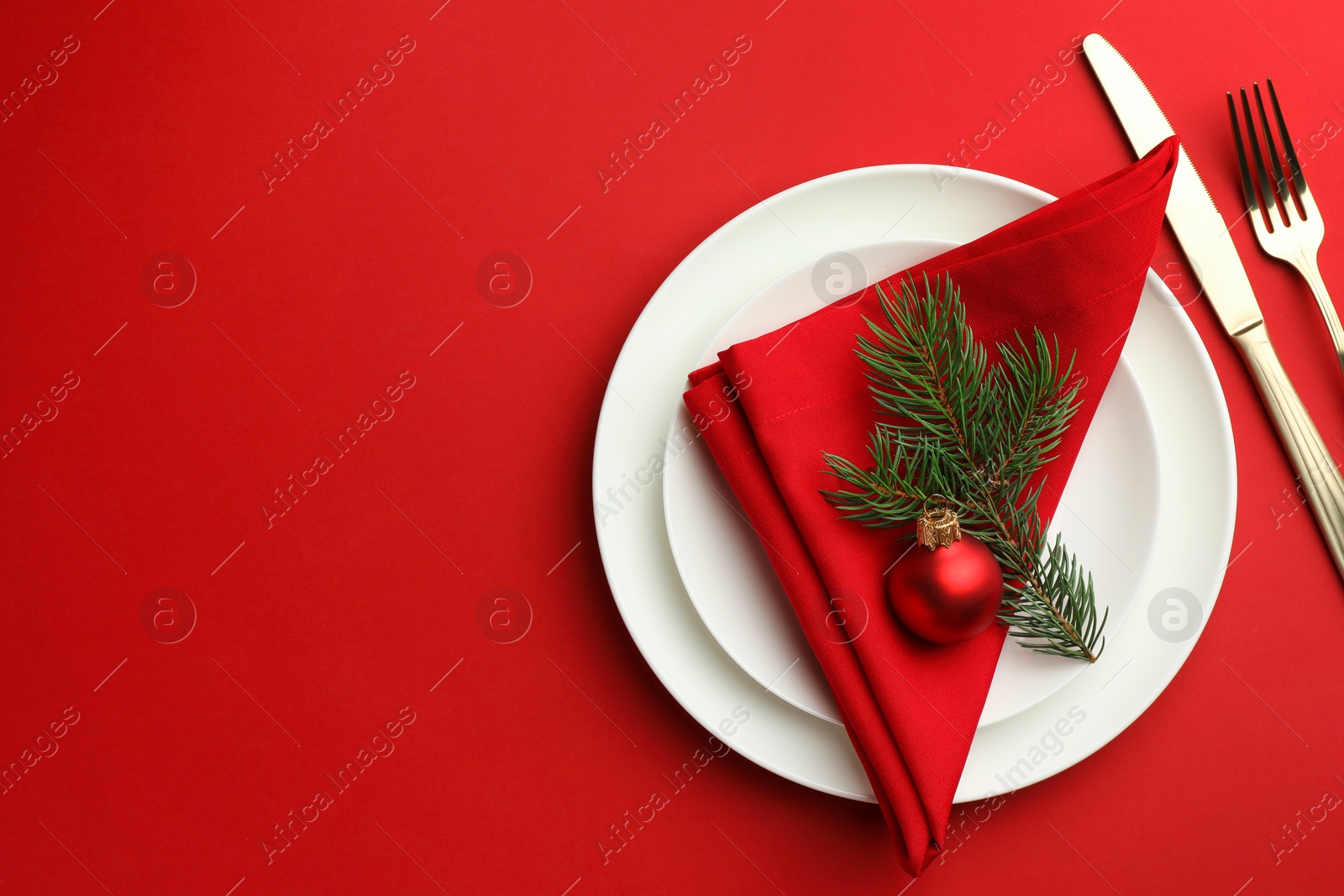 Photo of Beautiful Christmas setting with plates, elegant cutlery and festive decor on red table, flat lay. Space for text