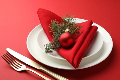 Photo of Beautiful Christmas setting with plates, elegant cutlery and festive decor on red table