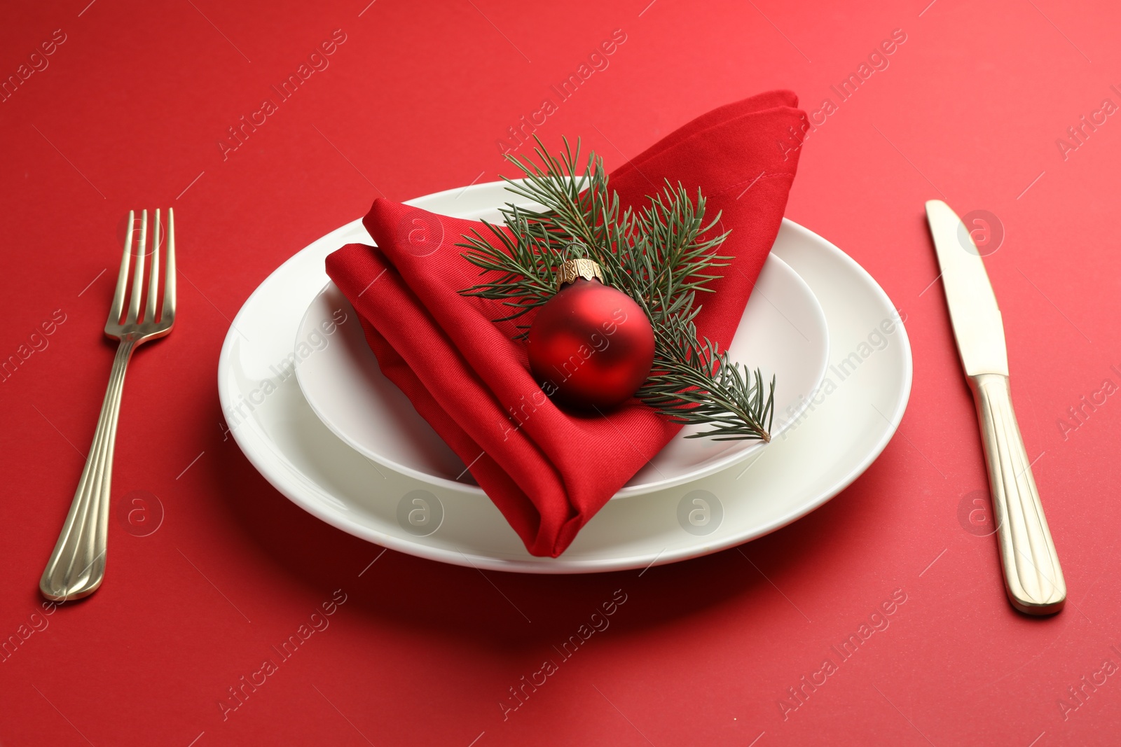 Photo of Beautiful Christmas setting with plates, elegant cutlery and festive decor on red table