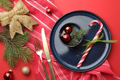 Photo of Beautiful Christmas setting with plate, elegant cutlery and festive decor on red table, flat lay