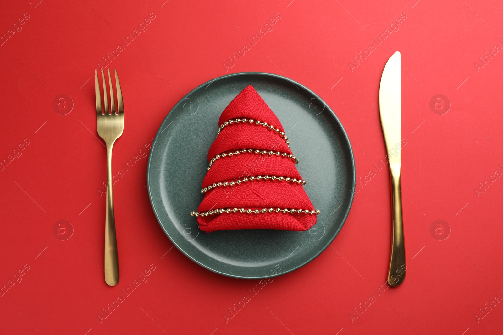 Photo of Beautiful Christmas setting with plate, elegant cutlery and festive decor on red table, flat lay