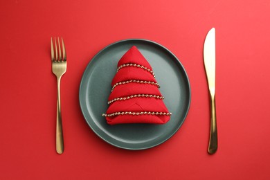 Photo of Beautiful Christmas setting with plate, elegant cutlery and festive decor on red table, flat lay