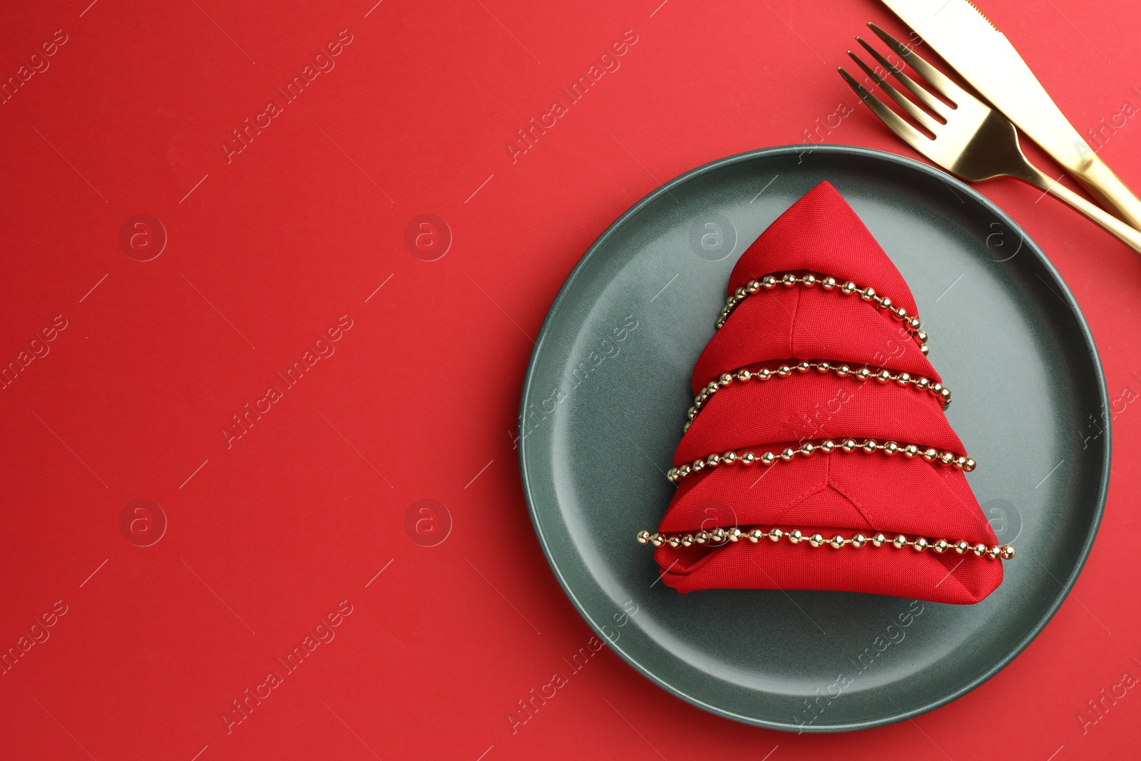 Photo of Beautiful Christmas setting with plate, elegant cutlery and festive decor on red table, flat lay. Space for text