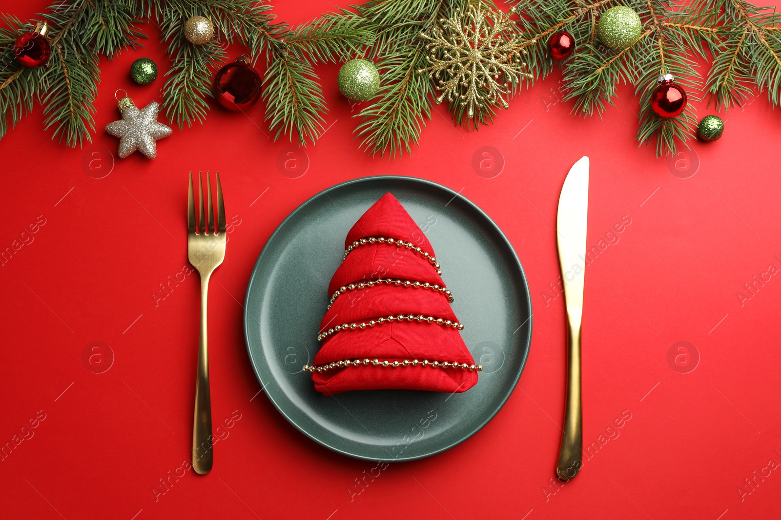 Photo of Beautiful Christmas setting with plate, elegant cutlery and festive decor on red table, flat lay