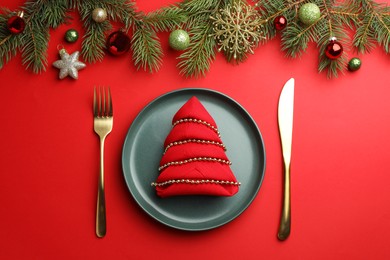 Photo of Beautiful Christmas setting with plate, elegant cutlery and festive decor on red table, flat lay