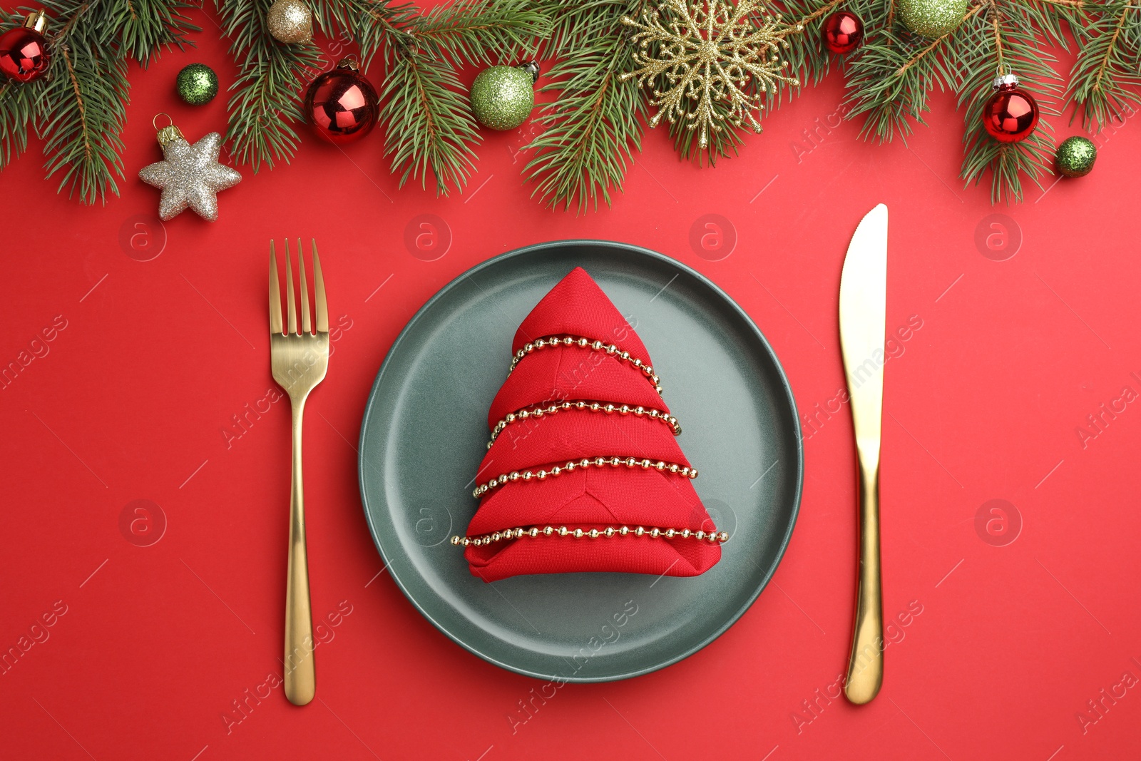 Photo of Beautiful Christmas setting with plate, elegant cutlery and festive decor on red table, flat lay