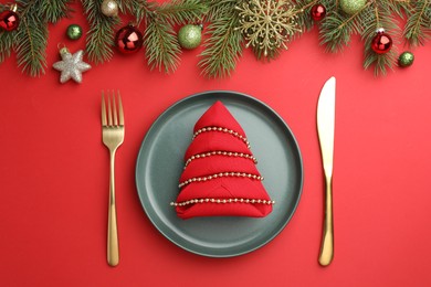 Beautiful Christmas setting with plate, elegant cutlery and festive decor on red table, flat lay