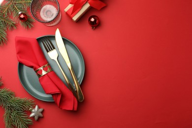 Photo of Beautiful Christmas setting with plate, elegant cutlery and festive decor on red table, flat lay. Space for text