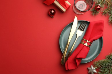 Photo of Beautiful Christmas setting with plate, elegant cutlery and festive decor on red table, flat lay. Space for text