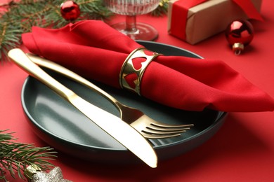 Photo of Beautiful Christmas setting with plate, elegant cutlery and festive decor on red table, closeup