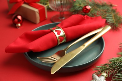 Photo of Beautiful Christmas setting with plate, elegant cutlery and festive decor on red table