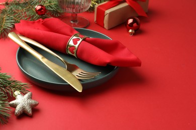 Photo of Beautiful Christmas setting with plate, elegant cutlery and festive decor on red table